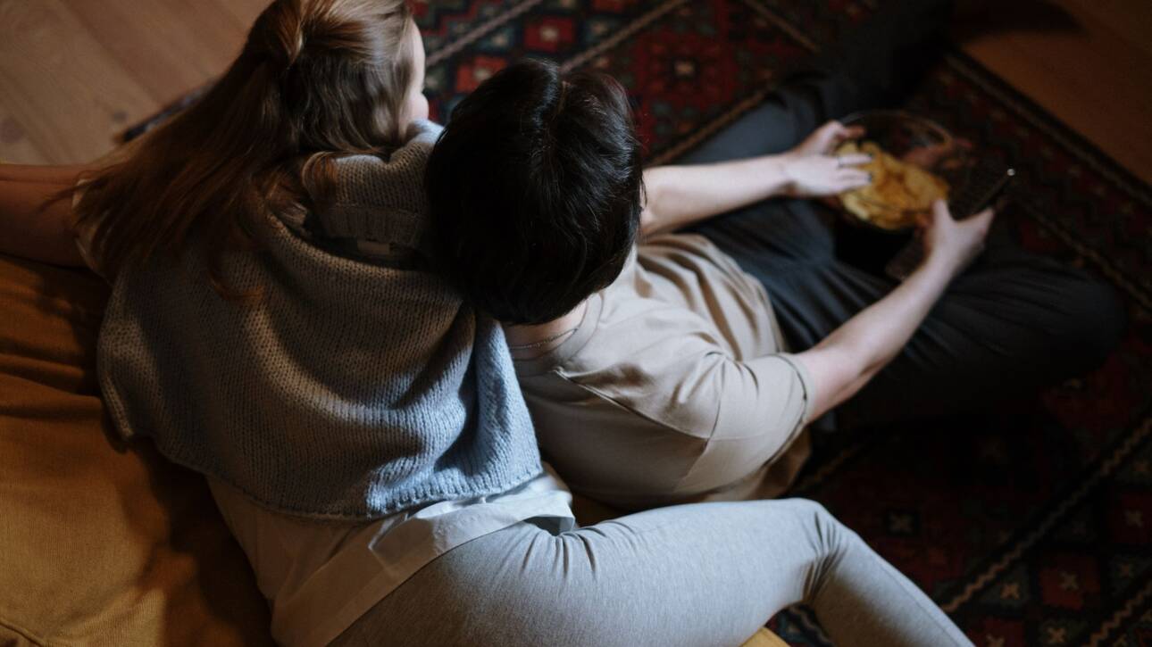 par i sofa, kvinde med mobiltelefon i hånden, afstand mellem to personer, rolig stue, vindue med aftenlys